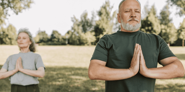 Ein älteres paar das Yoga im Freien macht.