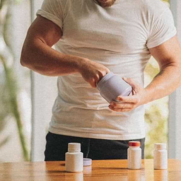 Mann öffnet eine Supplement-Dose, vor ihm stehen drei weitere Dosen auf einem Holztisch.