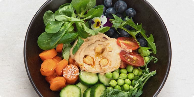 Bunte Bowl mit Hummus, Kichererbsen, Salat, Heidelbeeren, Tomaten, Erbsen, Gurke und Karotten.